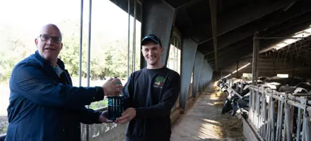 Ydelsestekniker Harmen Scholten Overrækker Gave Fra IDEXX – En Unikt Fremstillet Mælkejunge I Glas – Til Thomas Borrisholt